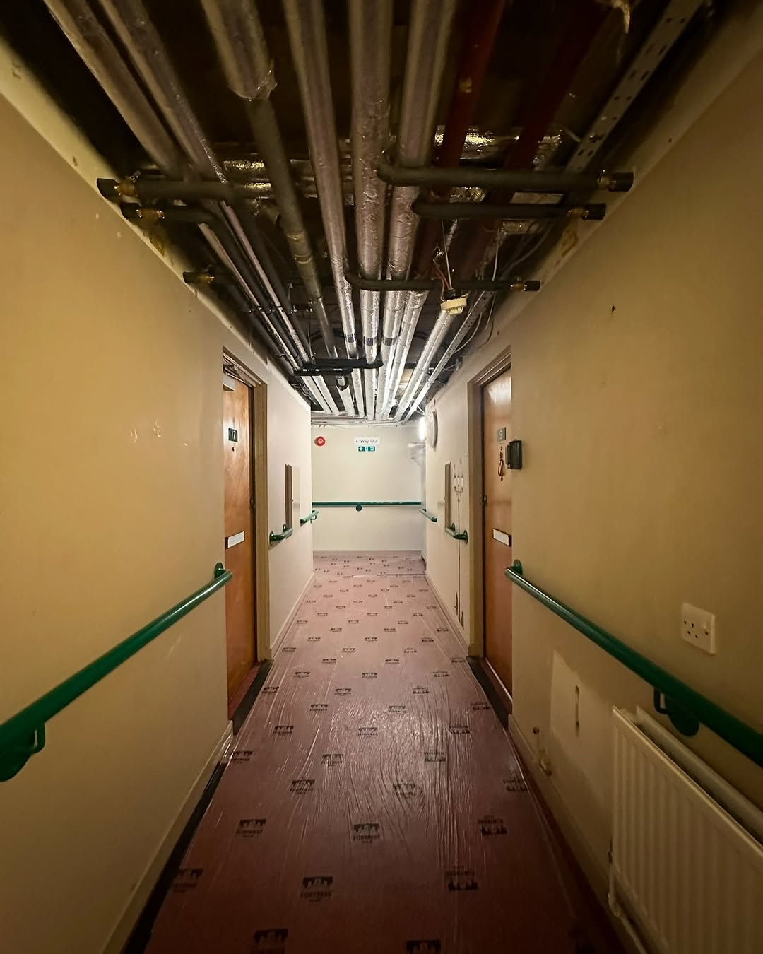 Insulated heating mains overhead in residential corridor with floor protection in place  -  occupied care home