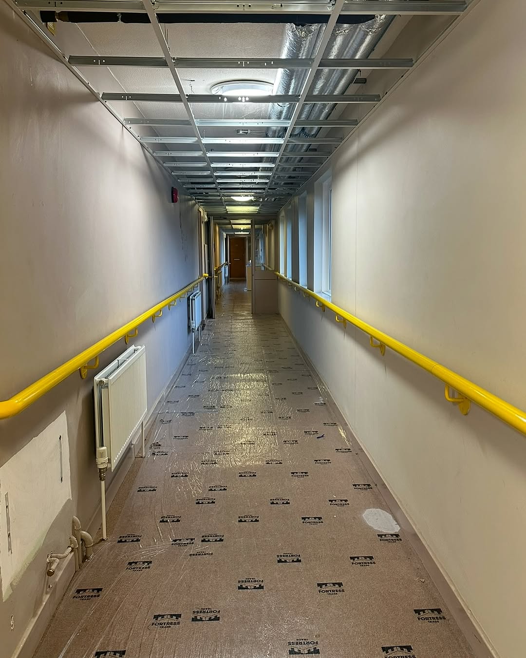 Near-complete corridor showing suspended ceiling grid, new radiators and floor protection  -  Sheffield