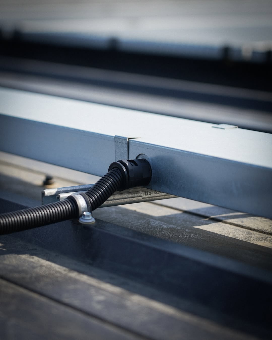 Close-up of corrugated conduit routed through aluminium mounting rail with cable gland fitting